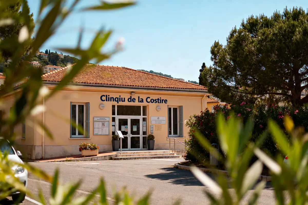 Façade de la Clinique de la Costire, entourée de végétation, sous un ciel bleu clair.