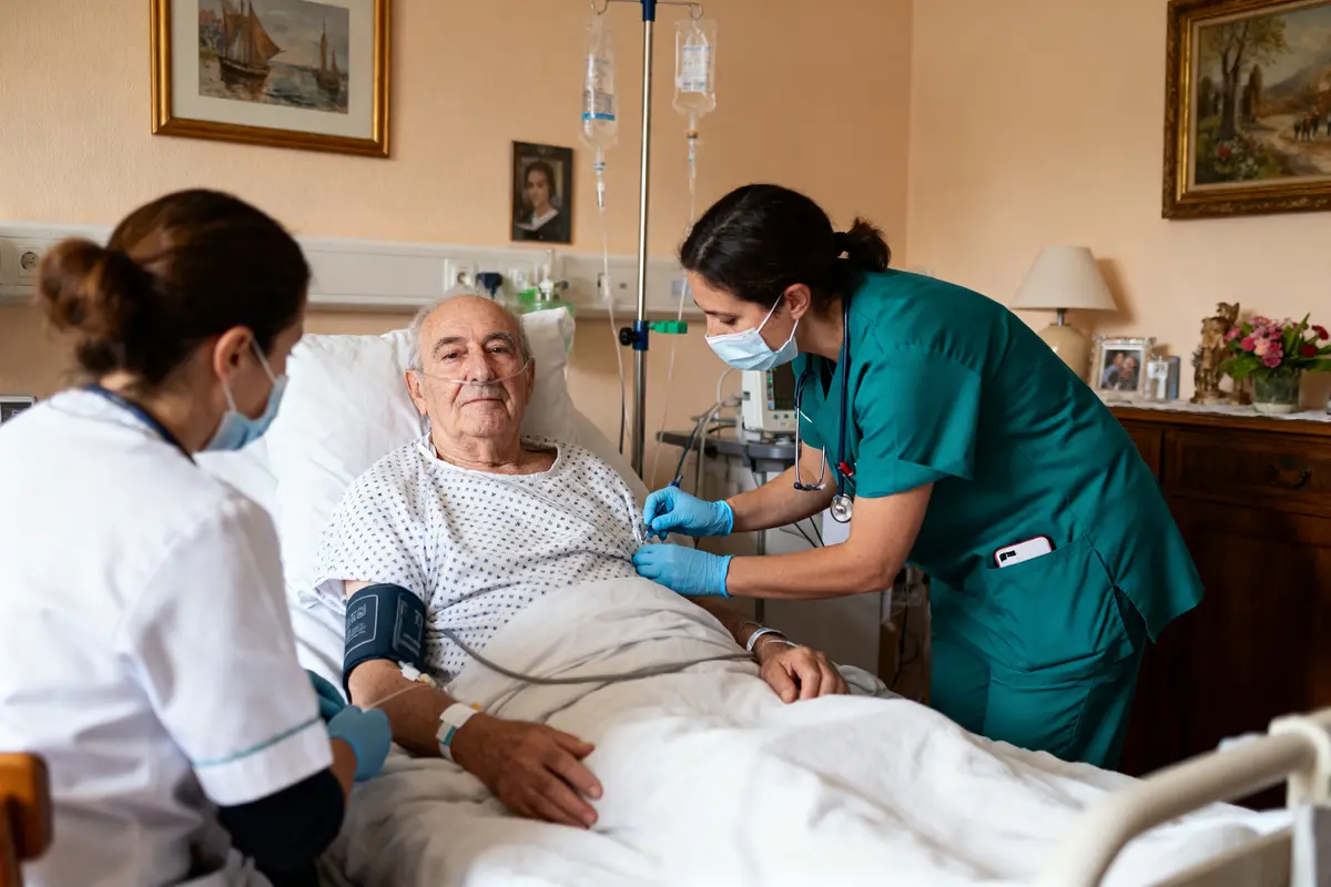 Un homme âgé reçoit des soins médicaux à l'hôpital, entouré de deux infirmières portant des masques.